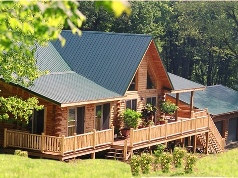 Custom log home with a green metal roof, large windows, and a wraparound deck