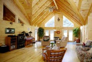 Log home living room with a vaulted pine ceiling, exposed timber trusses, and tall gable windows